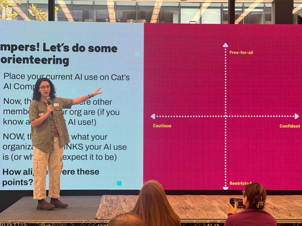 A woman stands on stage, recapping Beekeeper Group's 2025 day of purpose as she gestures toward a large screen showing text and a colorful chart labeled “Cautious–Confident” and “Restricted–Free-for-all,” while the audience watches attentively.