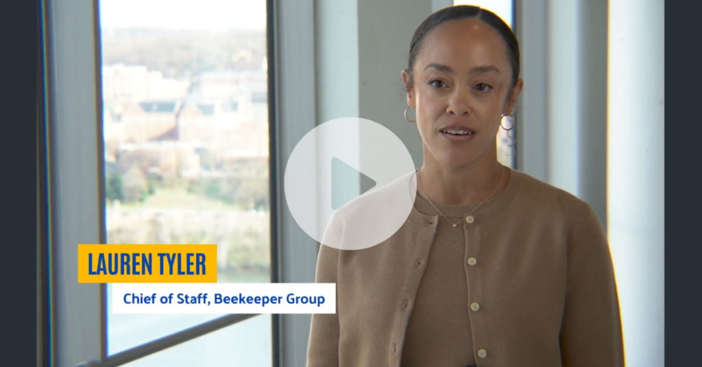 A woman stands indoors by large windows, cityscape behind her. On-screen text reads “LAUREN TYLER, Chief of Staff, Beekeeper Group.” A play button overlays the image, hinting at an annual recap from Beekeeper Group.