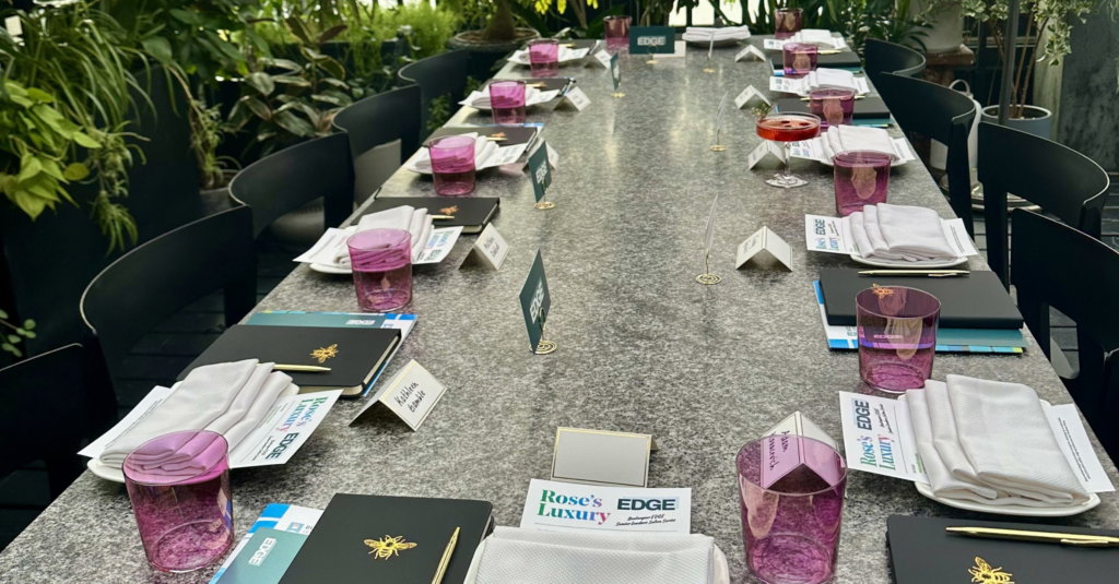 hive five graphics (19) A Hive Five dining table set for an event with place cards, black journals, white napkins, and pink glasses at each setting.